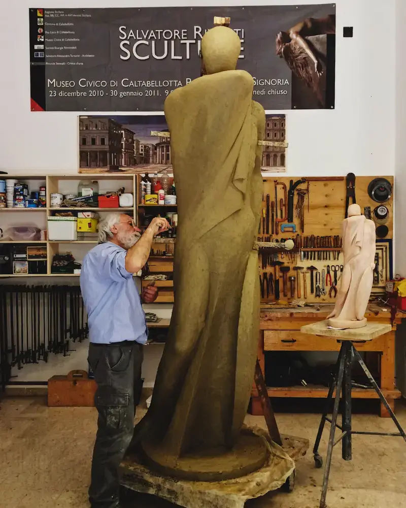 Salvatore Rizzuti scolpisce una grande figura in argilla nel suo studio, accanto a un modello in scala. Foto scattata per il Festival EOLiè – arte, letteratura e società.