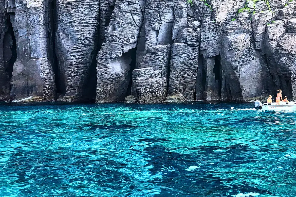 Scogliere basaltiche di Panarea con mare turchese trasparente e bagnanti in barca, Isole Eolie