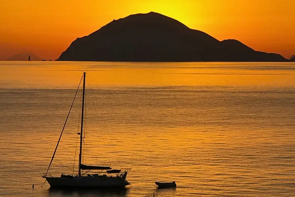 Filicudi vista al tramonto con una barca a vela in primo piano sul mare calmo delle Isole Eolie