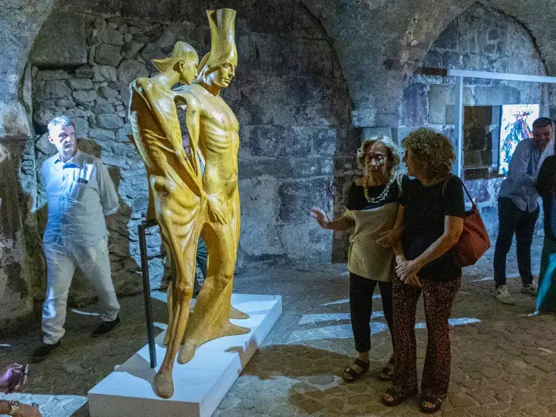 Visitatori osservano da vicino la scultura Canto delle Sirene 3 di Salvatore Rizzuti durante la mostra al Chiostro di Lipari