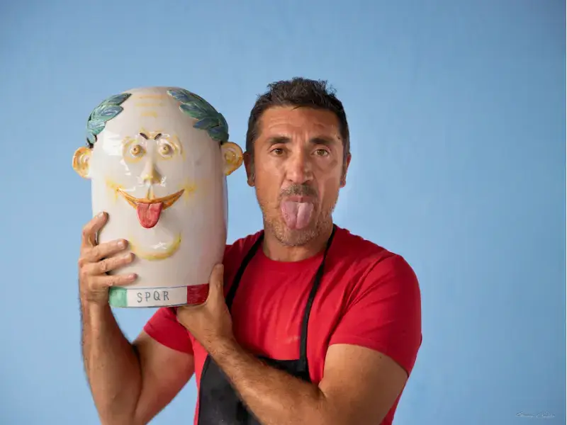 L’artista siciliano Nicolò Morales con una scultura in ceramica dal volto sorridente, posa ironica per il Festival EOLIé25.